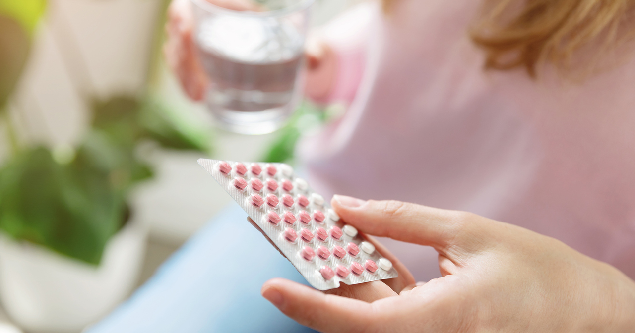Woman holding contraceptive pill and a glass of water