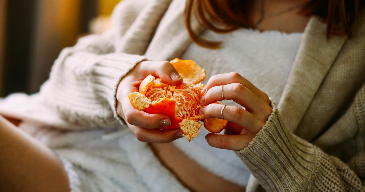 Close up of a comfortably dressed young woman peeling a bright orange