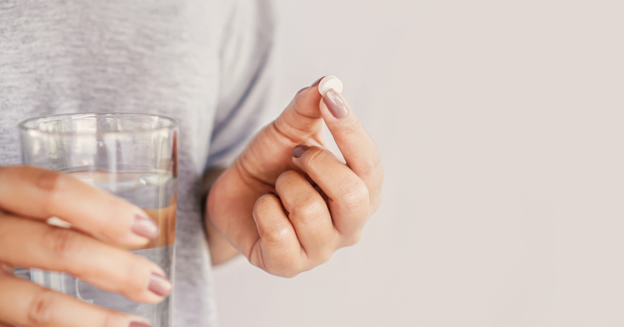 Close up of woman holding a pill in one hand and a glass of water in the other hand