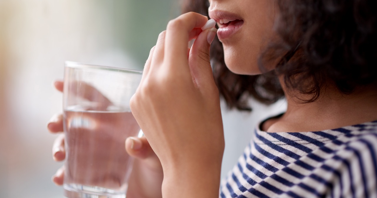 Close up of a young woman about to take a white pill, and holding a glass of water in her other hand