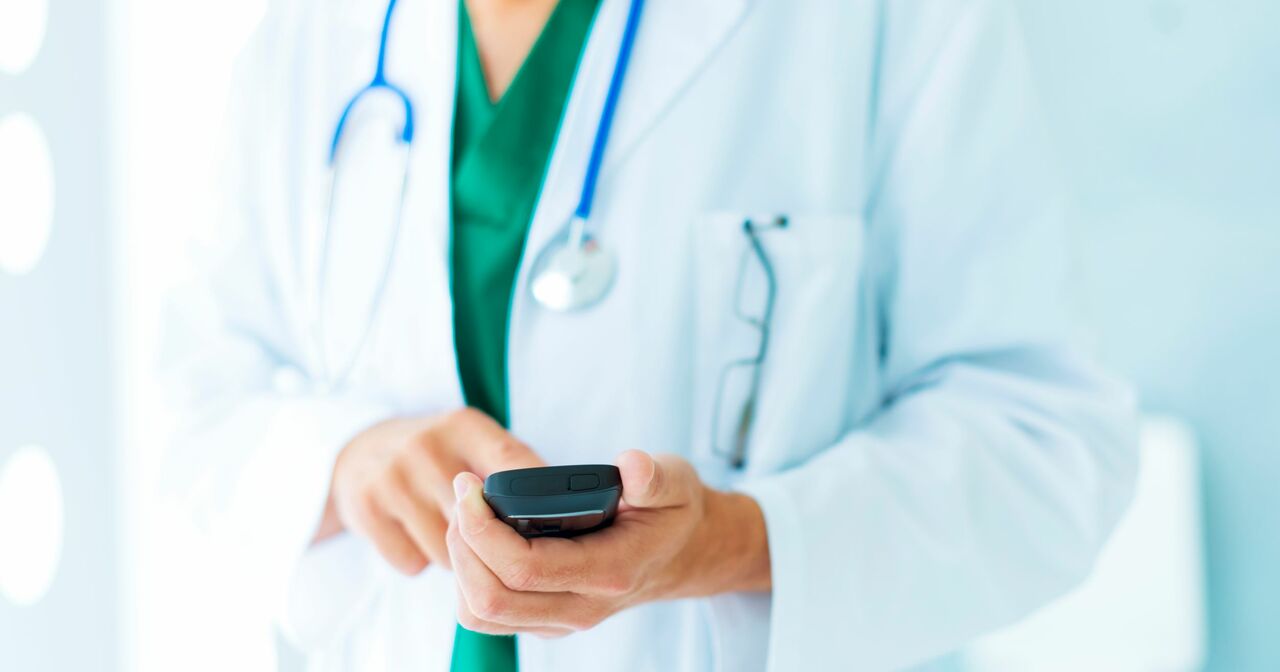 Close up of a doctor in a white coat, scrolling on their phone