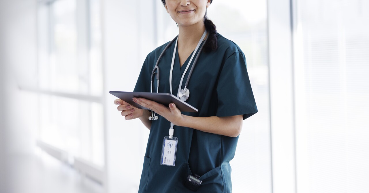 Smiling female provider in dark blue scrubs holding a digital tablet