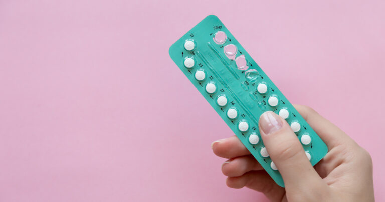 A woman holding birth control pills in teal packaging against a pink background