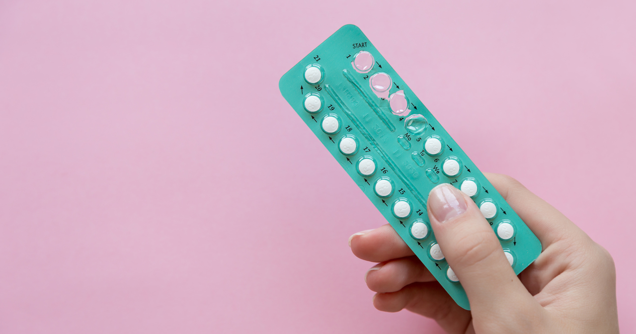 A woman holding birth control pills in teal packaging against a pink background