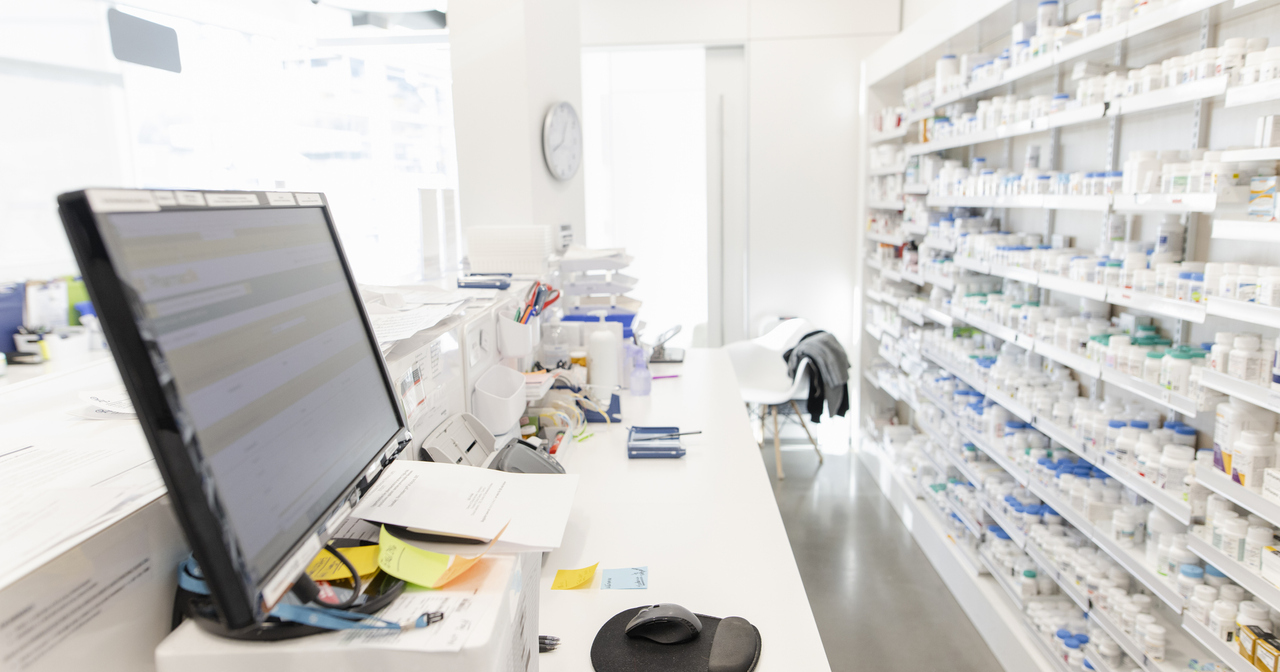 Computer and medications on shelves behind counter in a clean, bright pharmacy