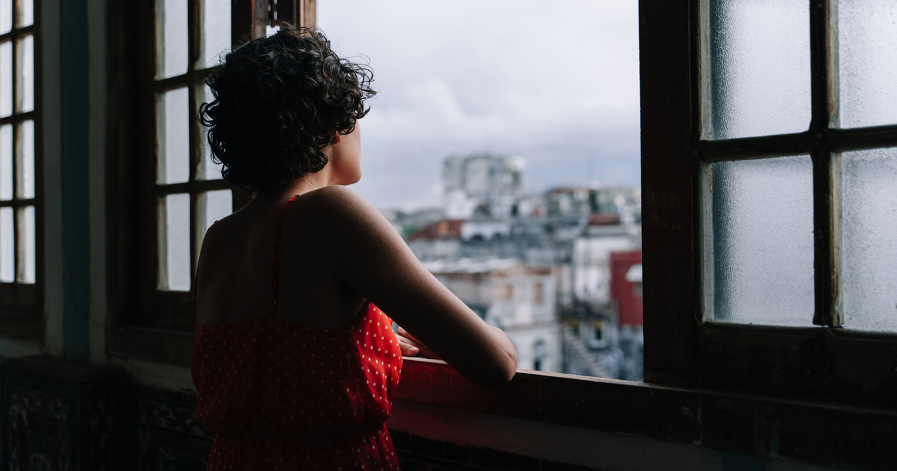 Young woman with curly hair in a red polka dot dress, looking out a window