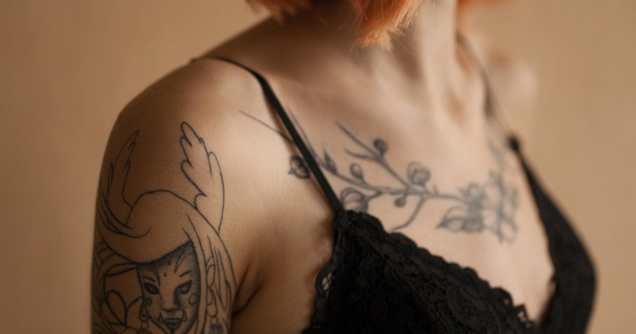 Close up of the shoulders of a red haired woman with tattoos in a lingerie top