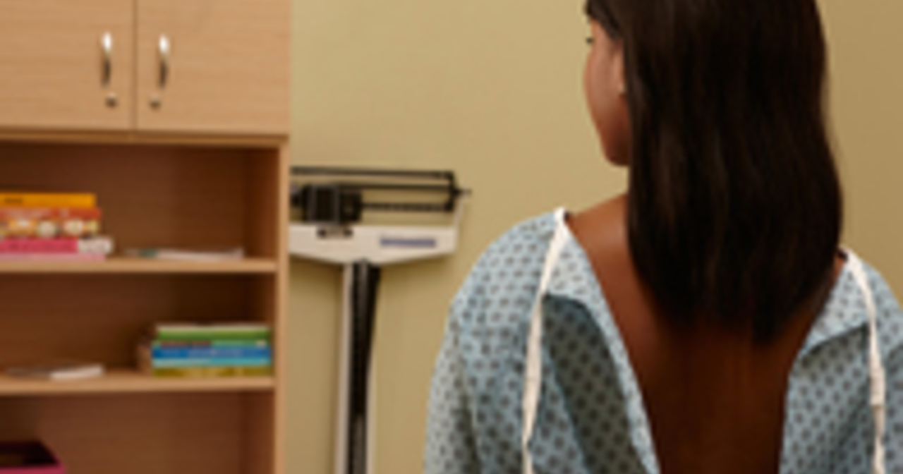 Back view of a woman in an exam gown waiting for the doctor