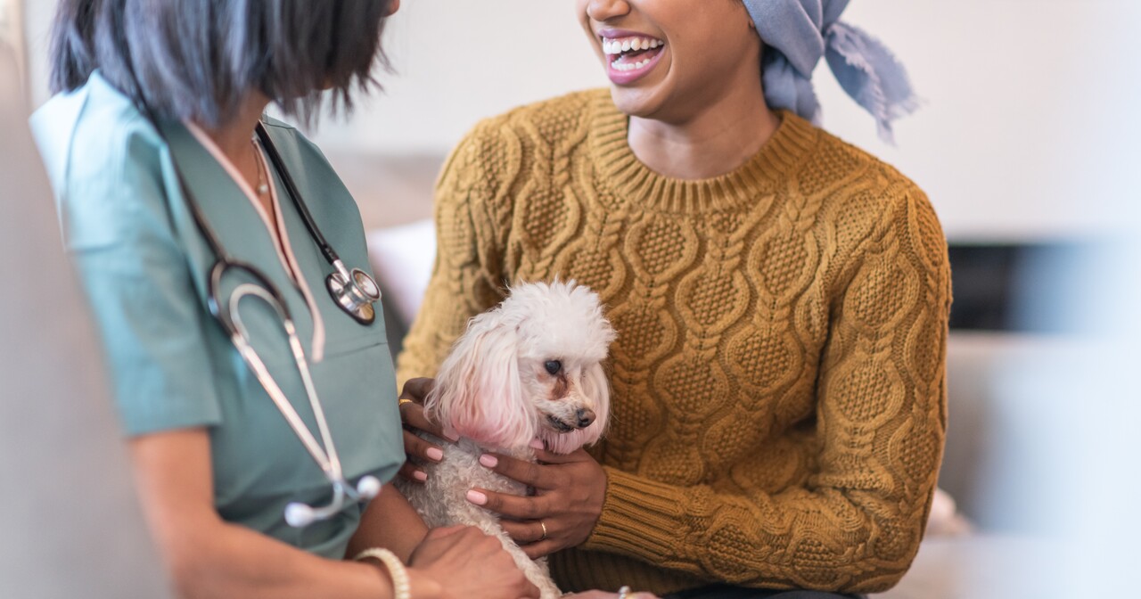Smiling patient in yellow holding a small white dog talking to a provider