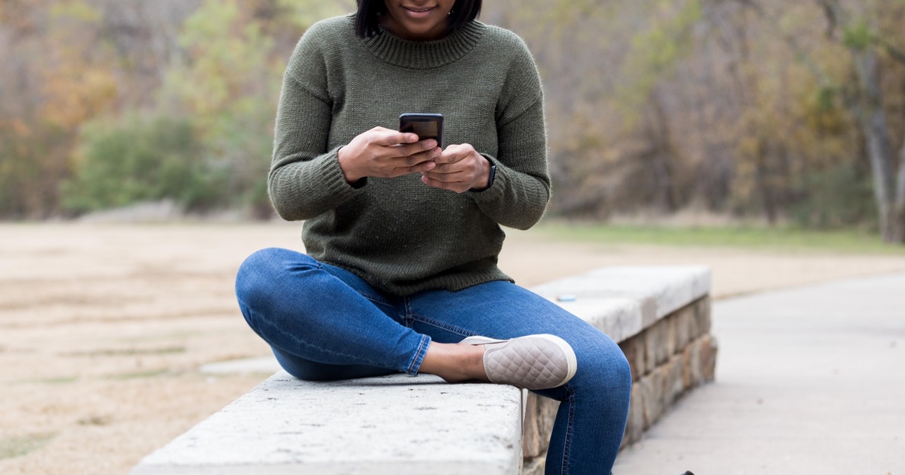 Young woman using phone, sitting on a ledge in a park