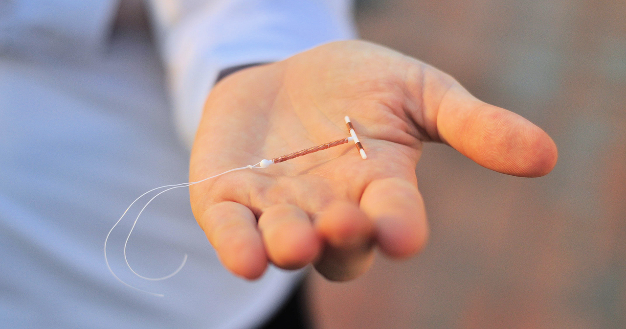 A close up of an open hand holding a copper IUD