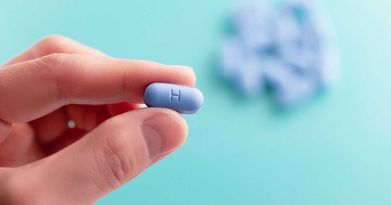 A close up of a hand holding a blue PrEP pill