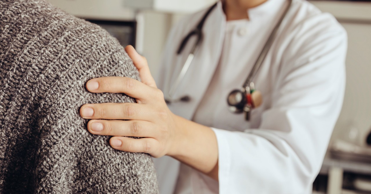 A close up of a doctor putting her hand on a patient's shoulder
