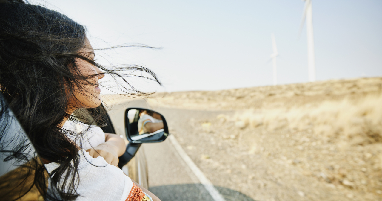 Smiling teenage girl with head out car window on desert road