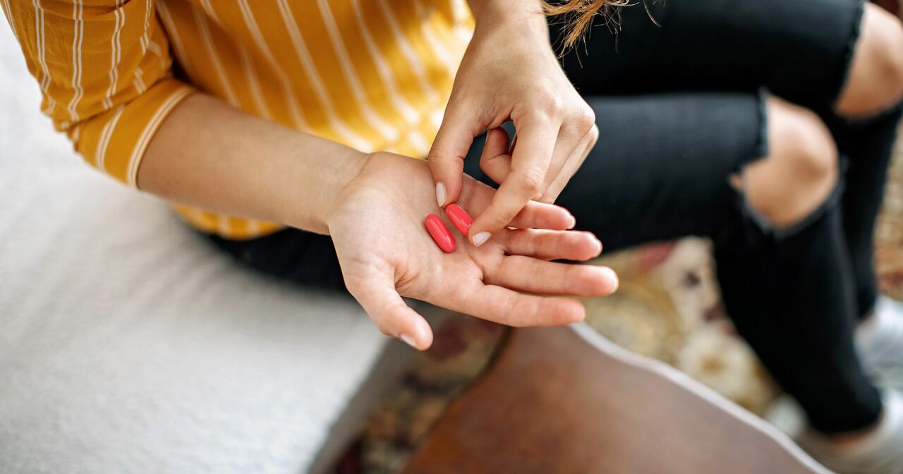 Woman holding two red pill in her open hand