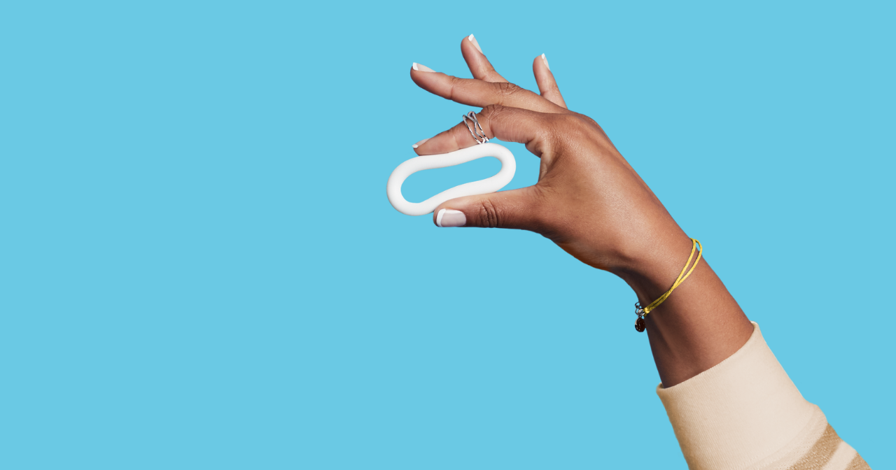 Close up of a hand holding the annovera birth control ring against a blue background