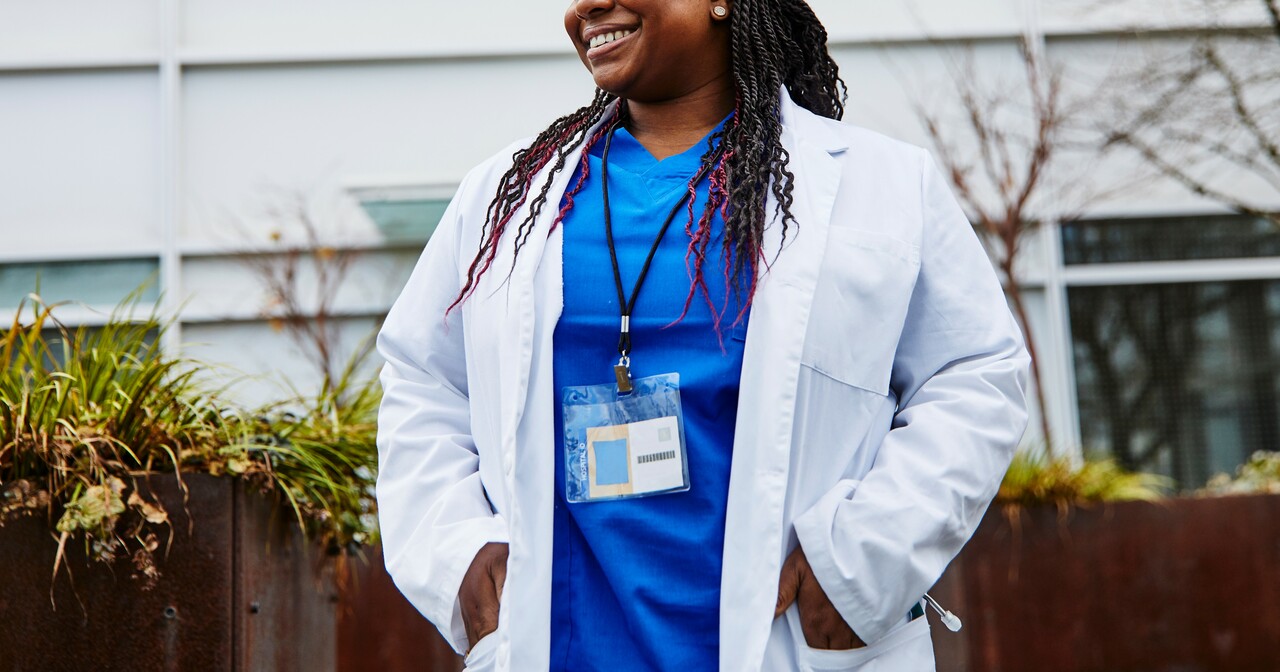 Smiling doctor standing outside with her hands in the pockets of her white lab coat