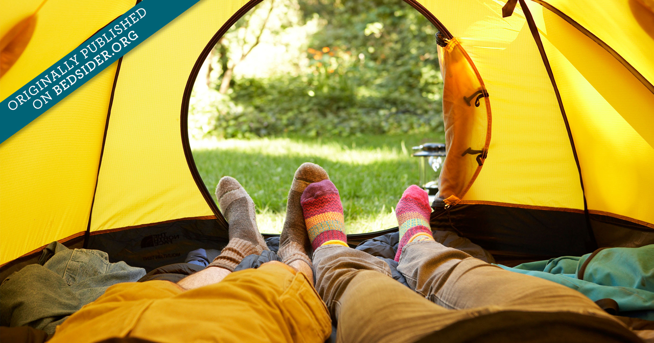 The feet of a couple in colorful socks laying side by side in a tent looking out the opening