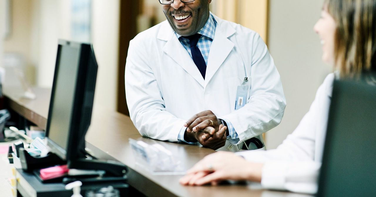 A smiling male provider chatting at the nurse's station