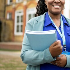A smiling woman holding a stack of blue educational books