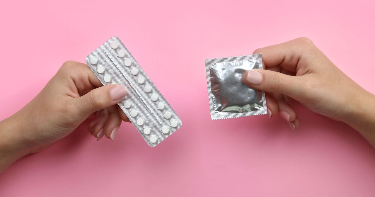 Close up of woman holding a pill pack in her left hand and a wrapped condom in her right hand