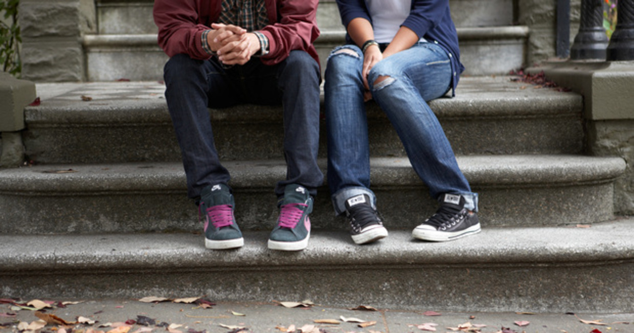 Close up of the legs of a young man and young woman sitting on a stoop